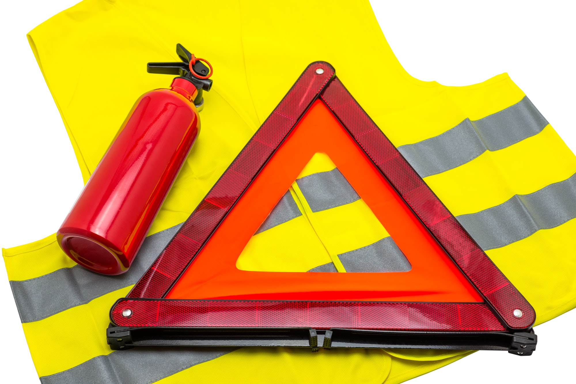 The fire extinguisher and reflective warning triangle lie on the reflective vest, isolated on a whit