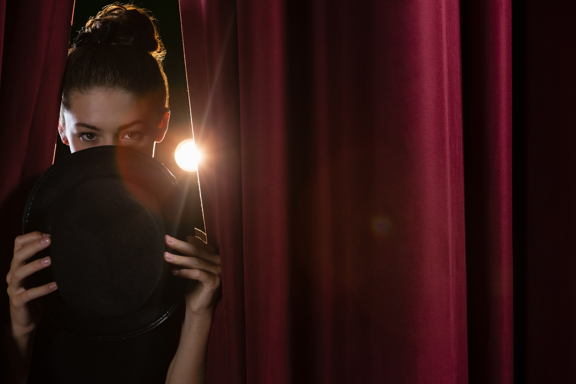 Ballet dancer with hat peeking through a stage curtain
